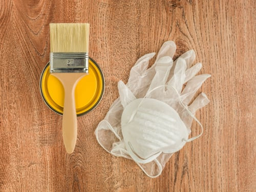 Paint brush, roller, gloves, and protective mask laid out on a wood workbench before an AR Interiors Decoration project