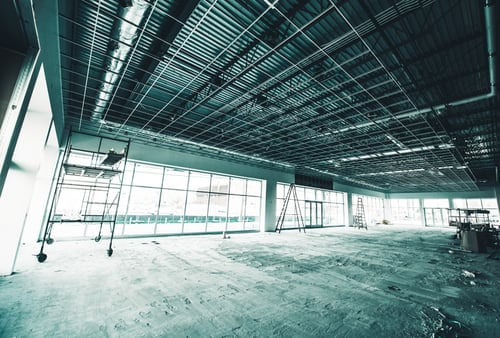 Open commercial interior build-out with exposed ceiling grid and glass storefront ready for painting