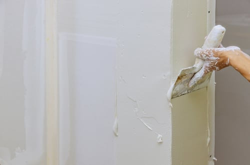 Drywall compound being smoothed onto a wall seam with a taping knife by an AR Interiors Decoration Inc finisher