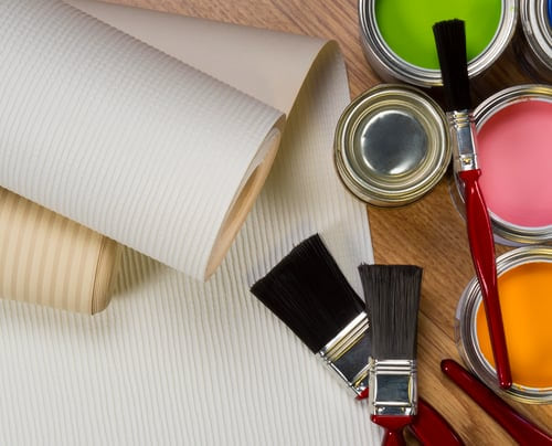 Rolls of wallpaper, open paint tins, and brushes arranged on a wood surface